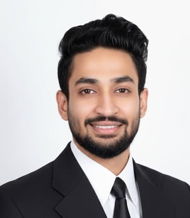 Professional headshot of a smiling bearded man in a black suit against a white background.