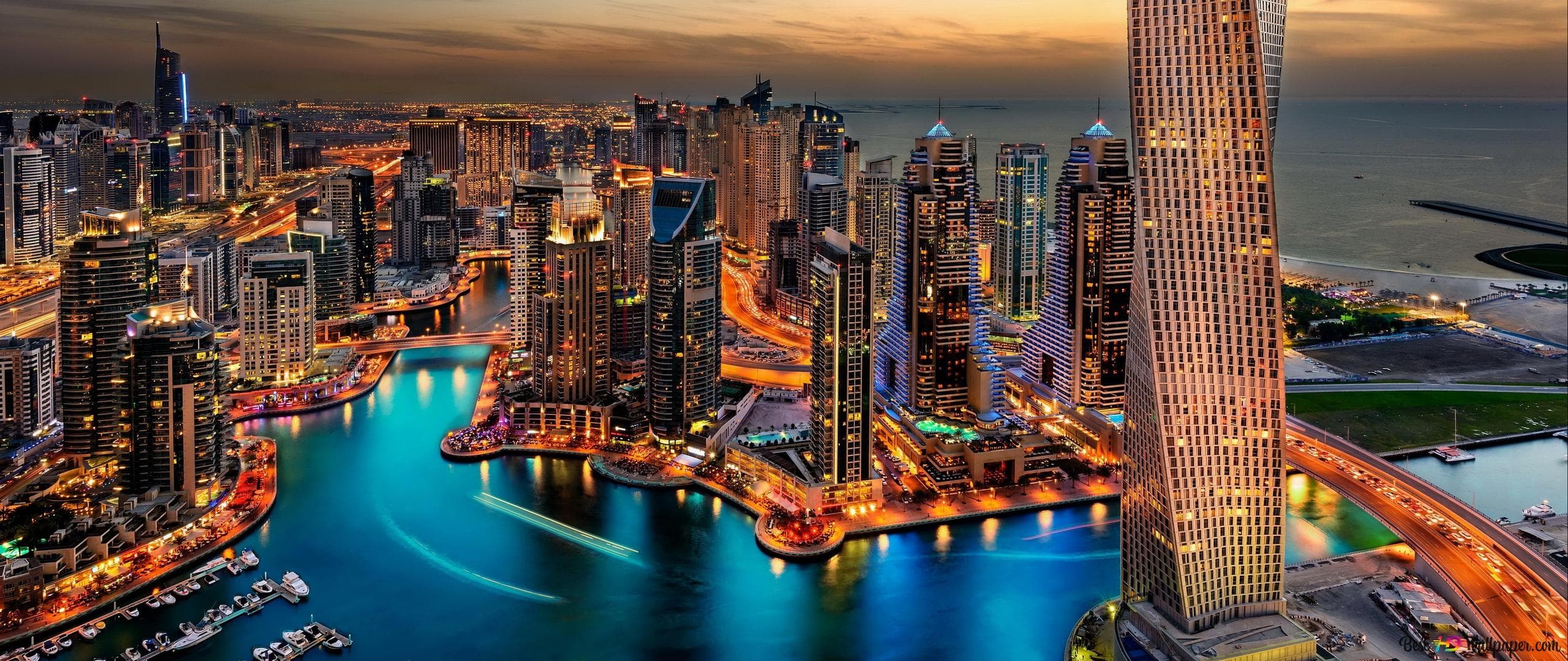 Illuminated Dubai Marina skyscrapers and twisted tower at dusk, reflecting in vibrant blue water.
